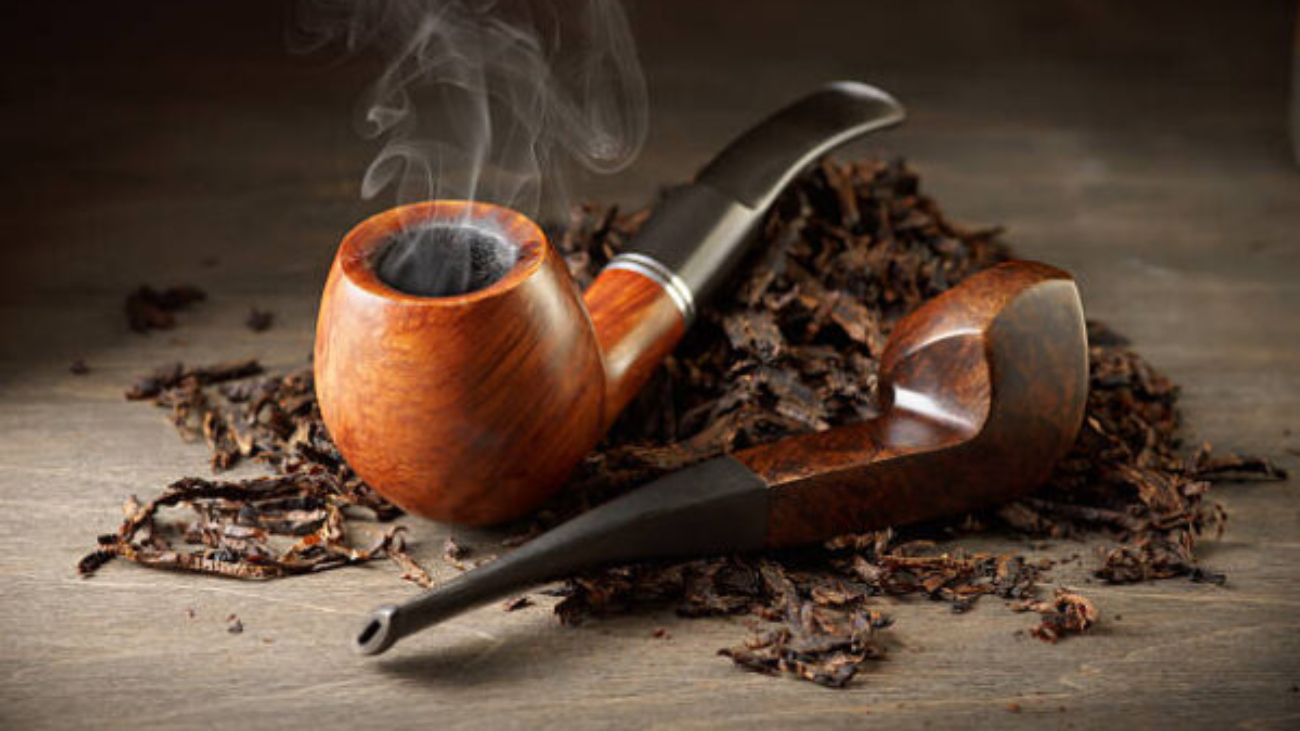 Two wooden pipe with smoke and tobacco pile on vintage wood.